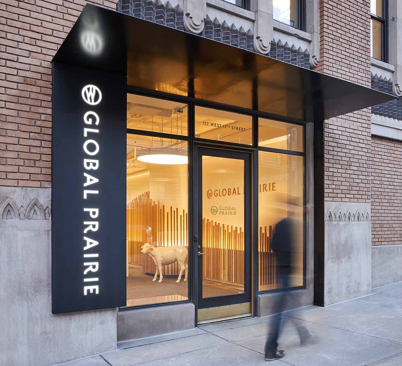Brick building with a black awning and entry way into the Global Prairie office in KC, a blurred man is walking past the door